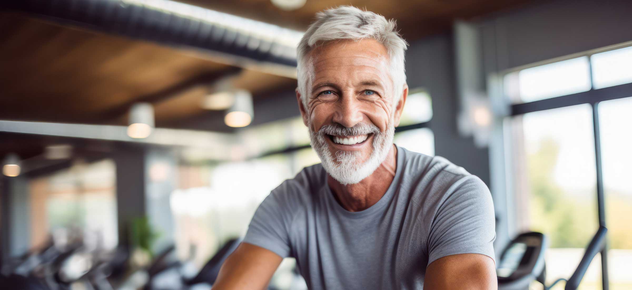 A gray-haired man smiles on a treadmill at a gym.