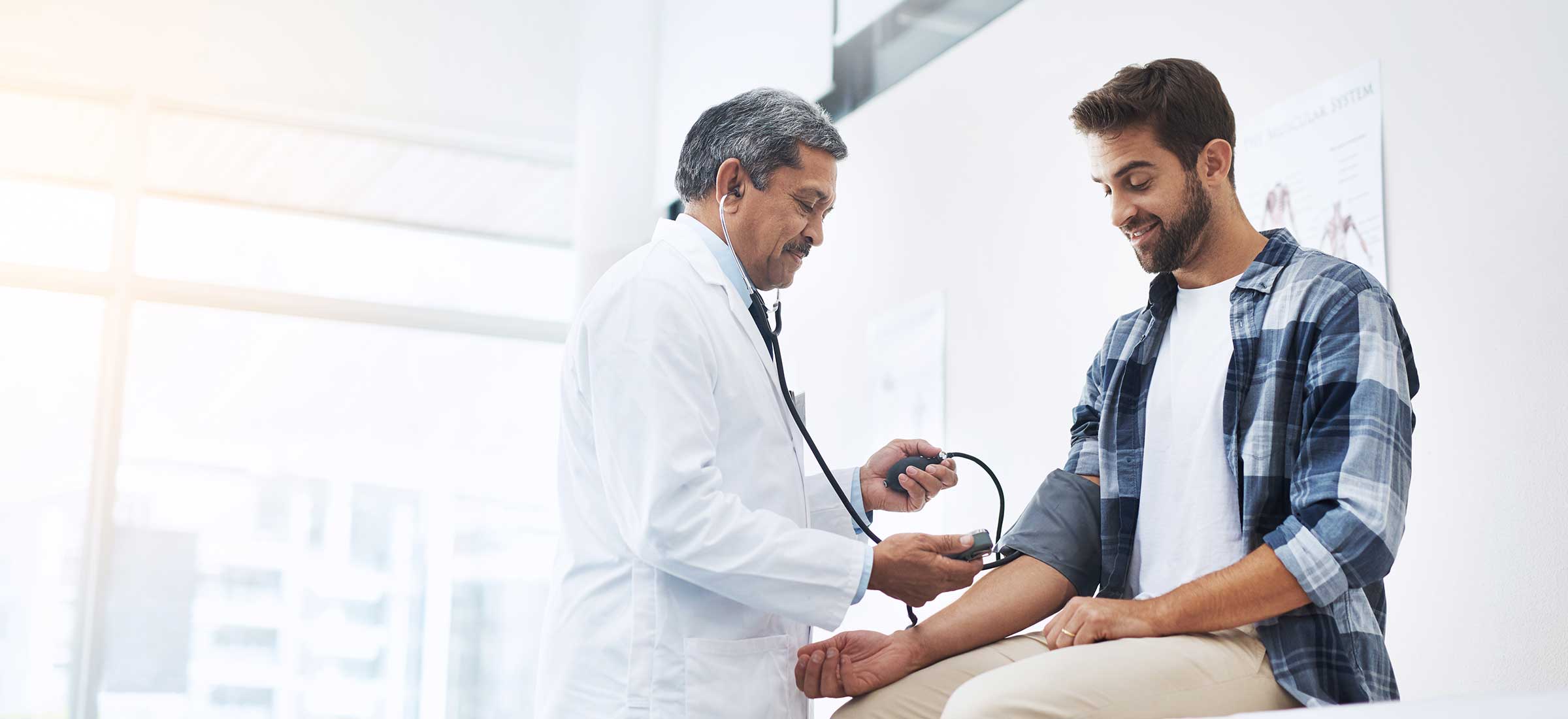 A male doctor checks the blood pressure of a male patient.