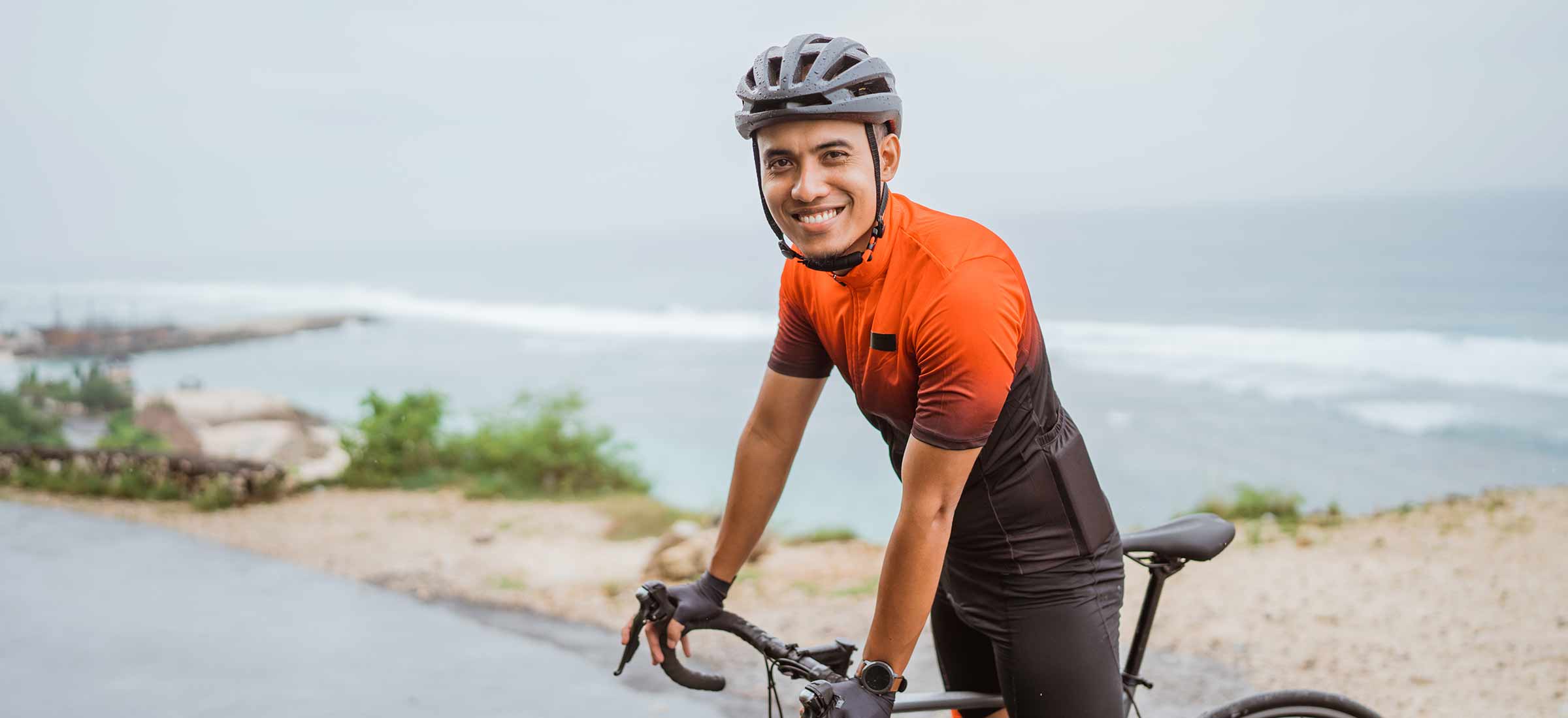 Male asian cyclist with red and black jersey standing on his bike.