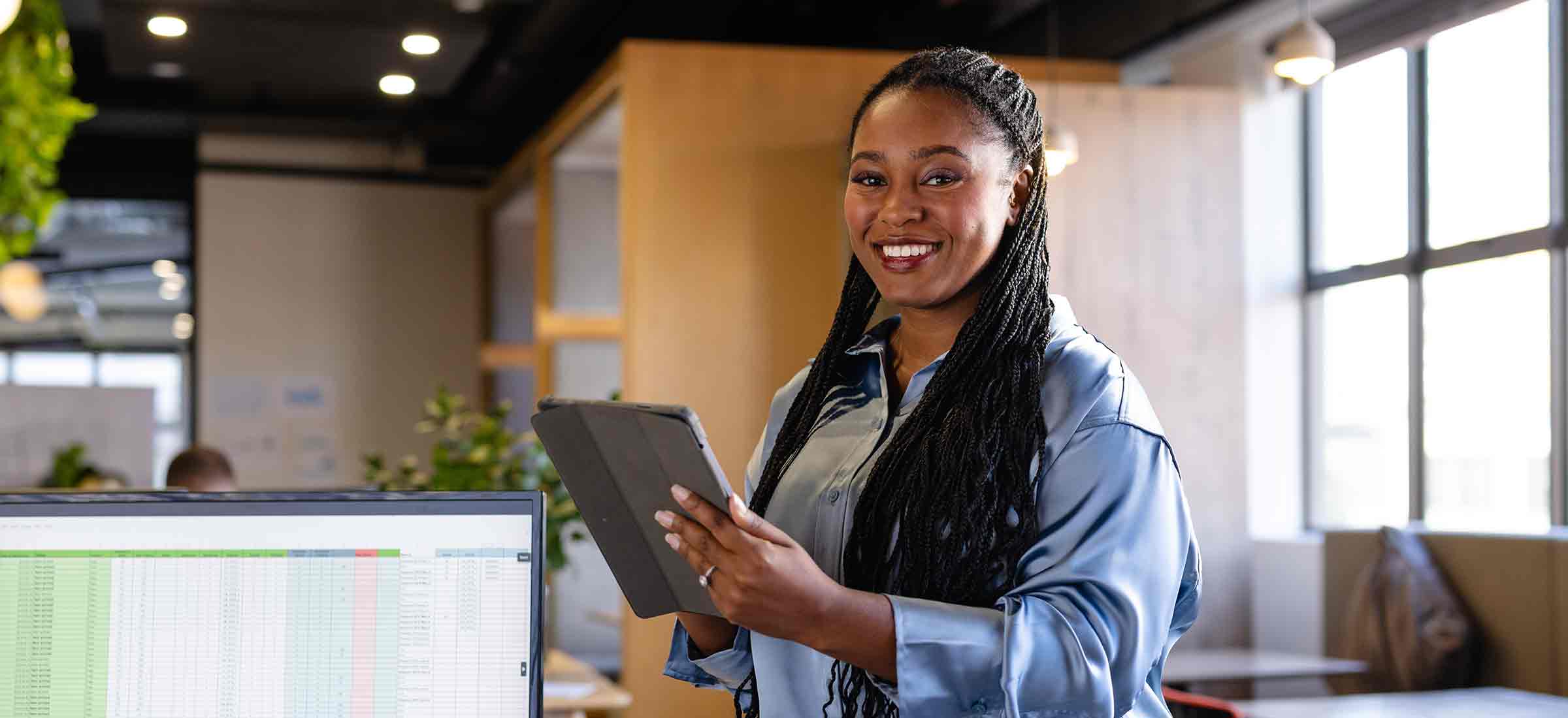 Portrait of happy African-American woman in casual businesswear using a tablet in an office.