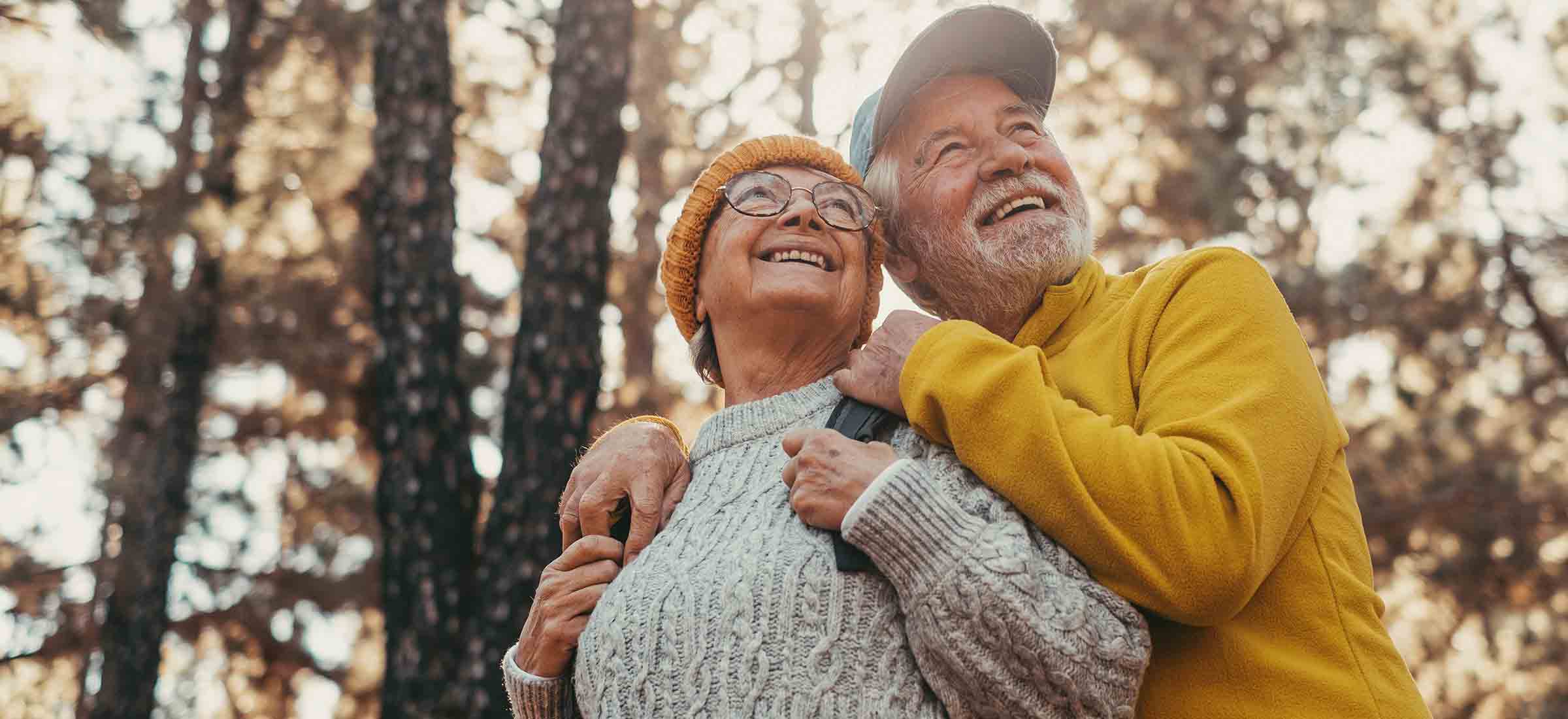 Close up photo of middle age cheerful people smiling and looking at the the trees of the forest around them.