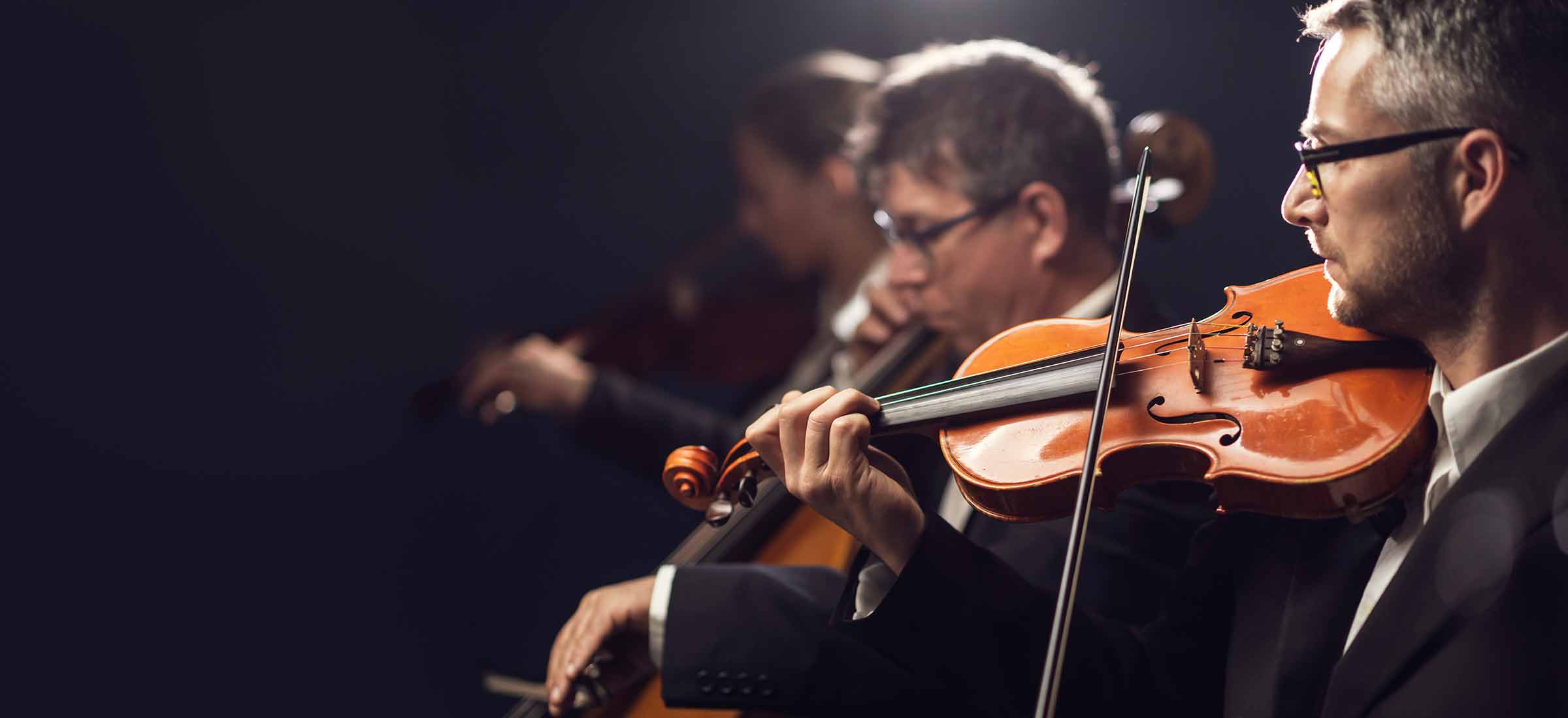 Orchestra musicians playing the violin and cello on stage during a classical music concert performance.