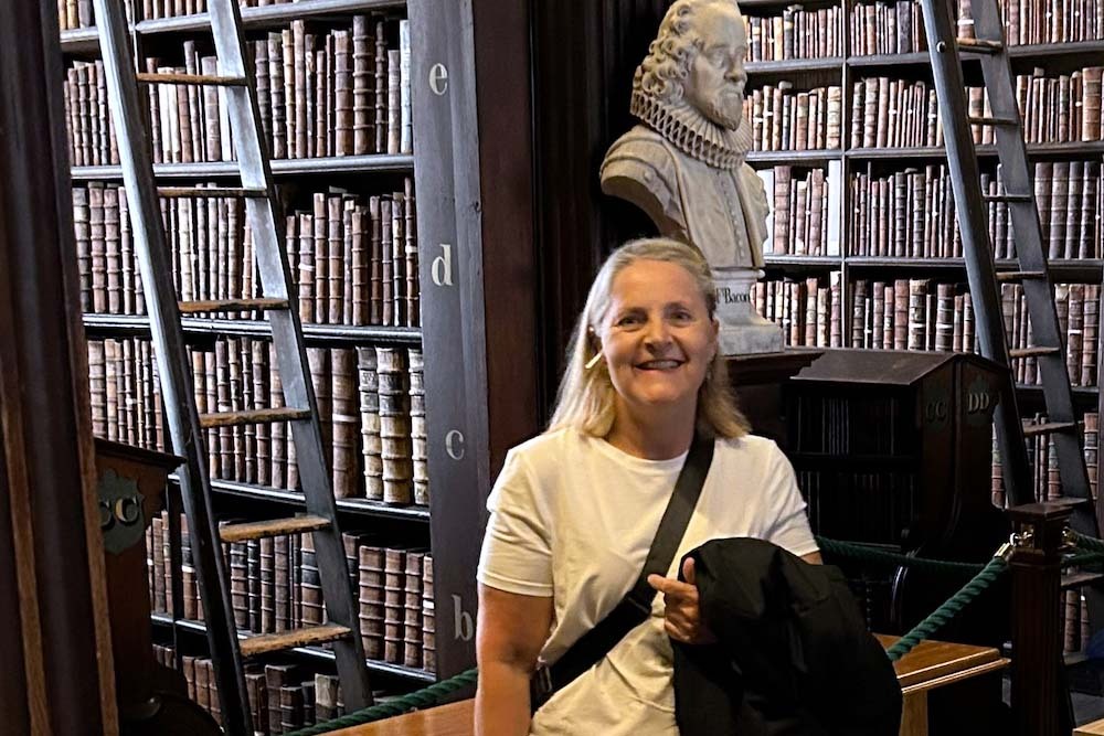 Glioblastoma patient Della Gallagher smiles in a library in Northern Ireland, in front of a wall of books