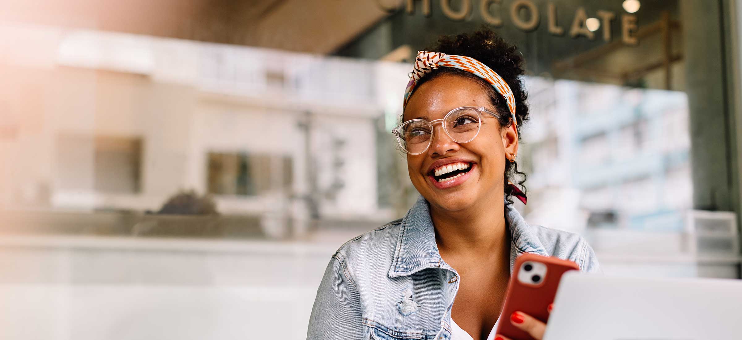 Happy female student sitting in a coffee shop, using a smartphone.