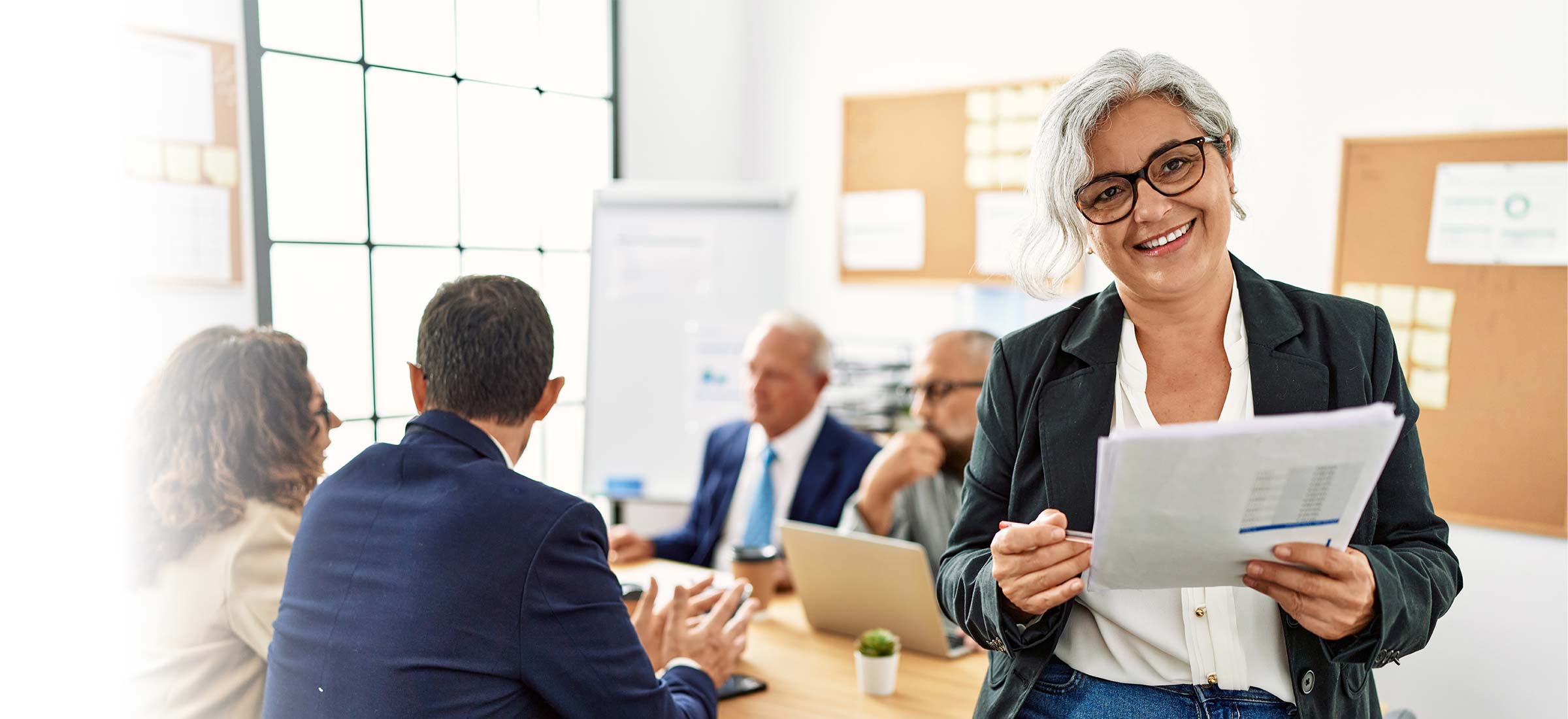 Person holding a stack of papers while in a meeting with four other people