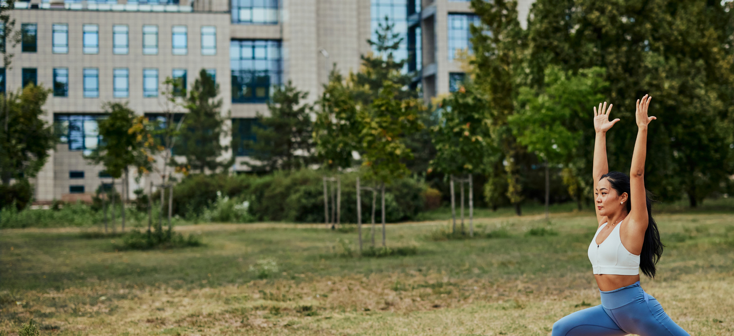 Young Asian woman exercising outdoors in a park, stretching her arms and legs.