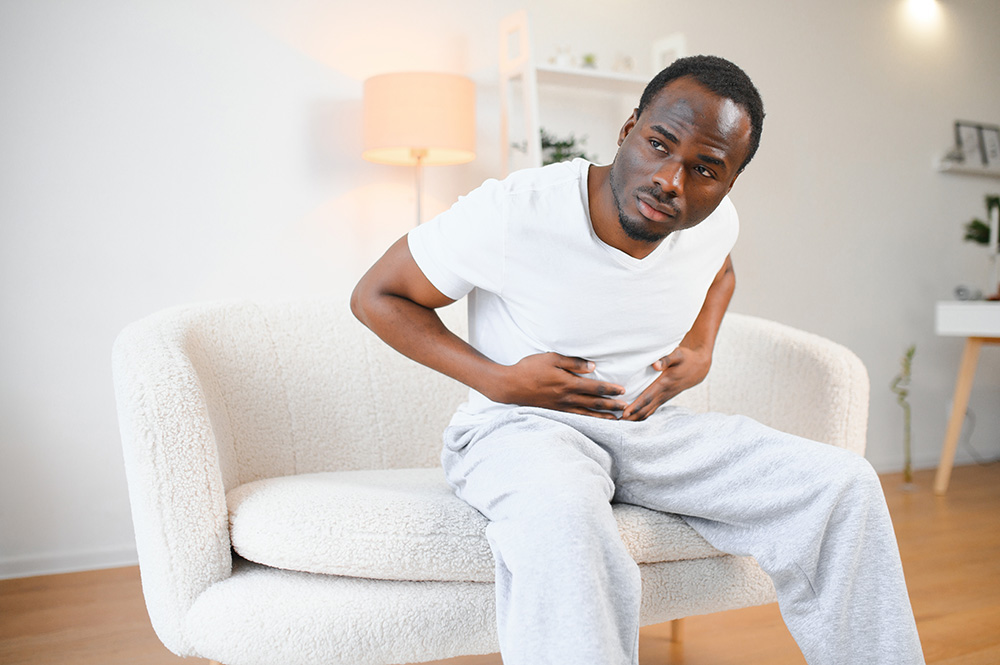 A young adult male leans forward and grabs his stomach and makes a face in pain.