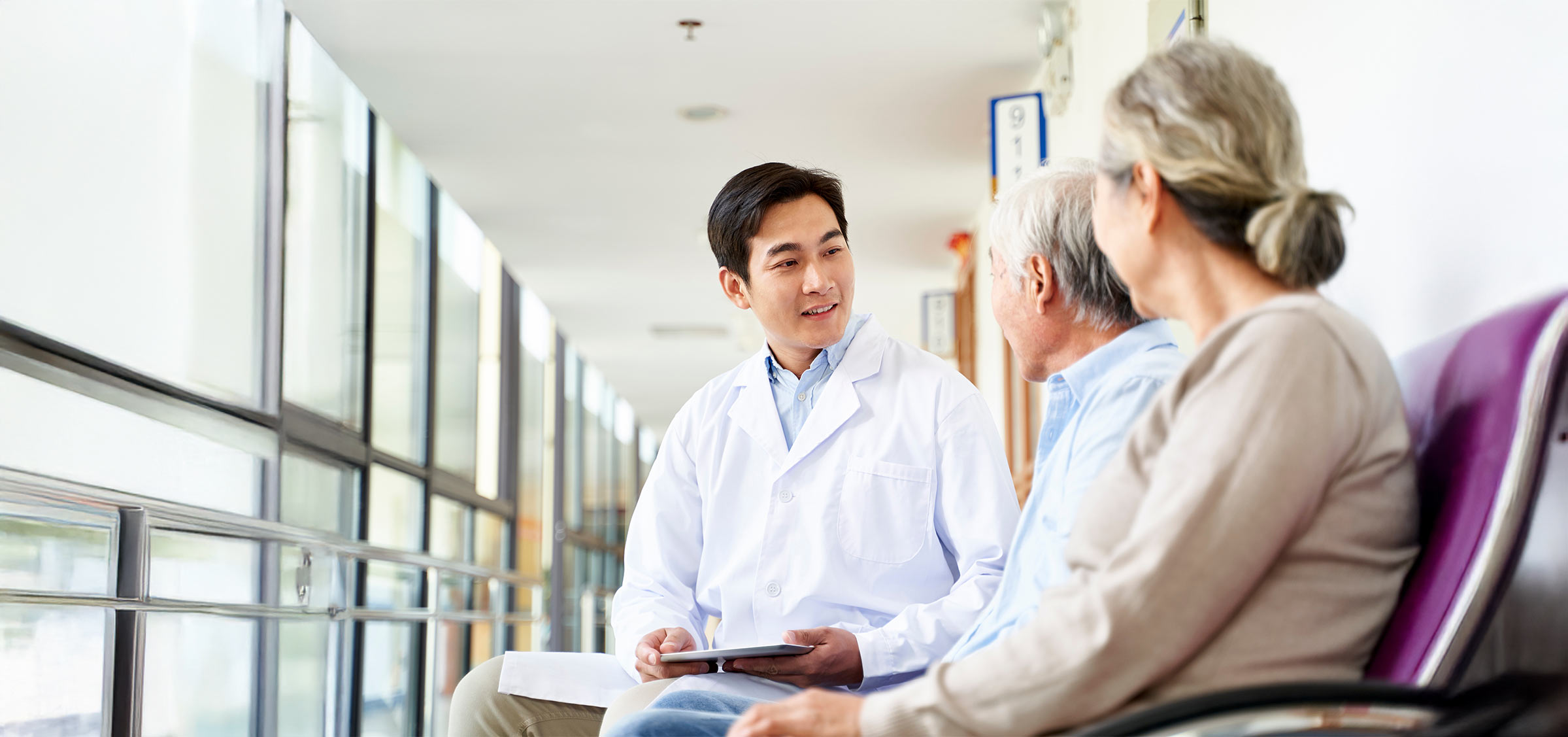 Young asian doctor talking to a senior couple in hospital hallway.