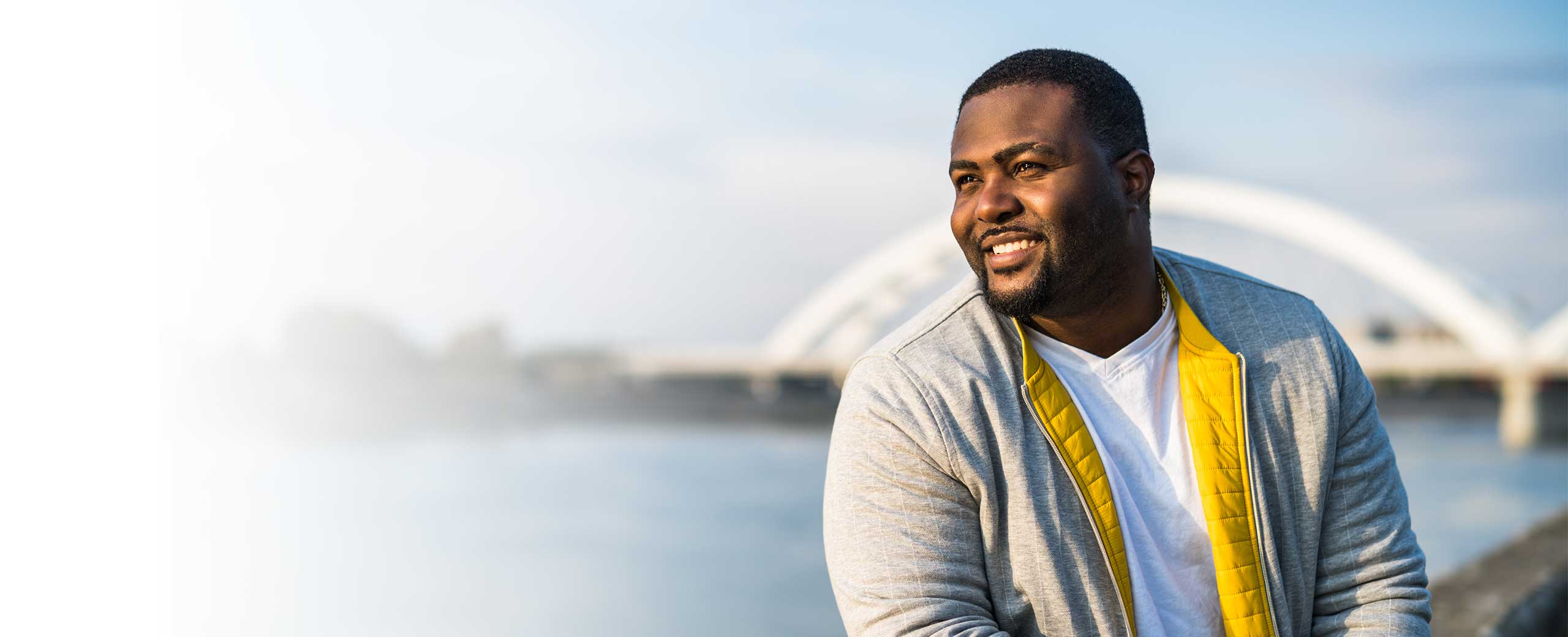 A man smiles beside a lake.