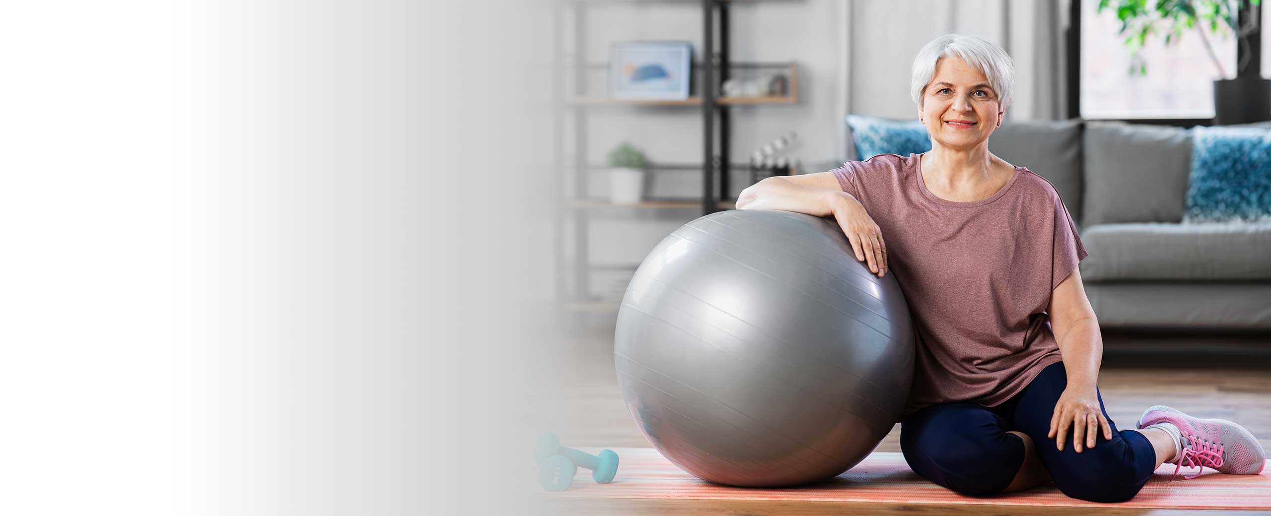 A woman sits on an exercise mat and leans on a ball.