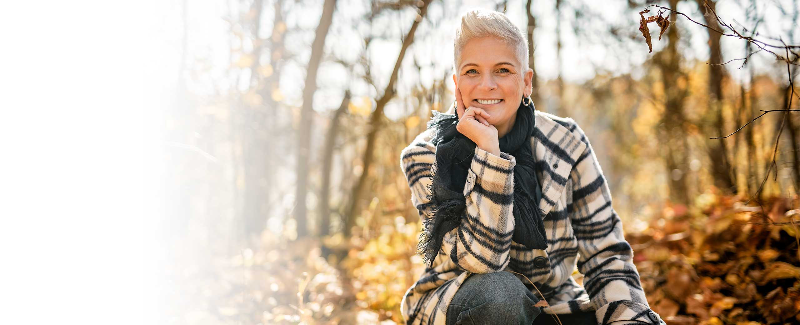 A woman smiles in the woods.